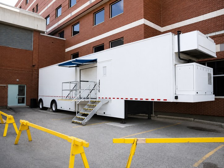 Conventional mobile MRI trailer parked beside a hospital with its staircase and canopy deployed